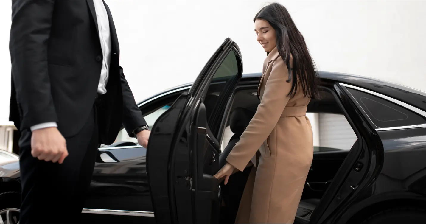 Woman entering luxury car with driver holding door.