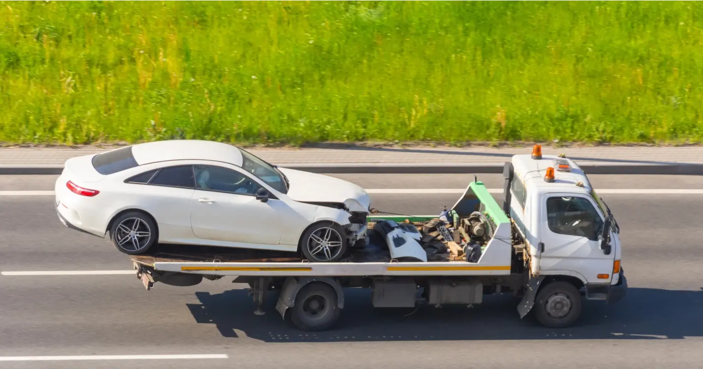 Tow truck hauling damaged white car on highway.